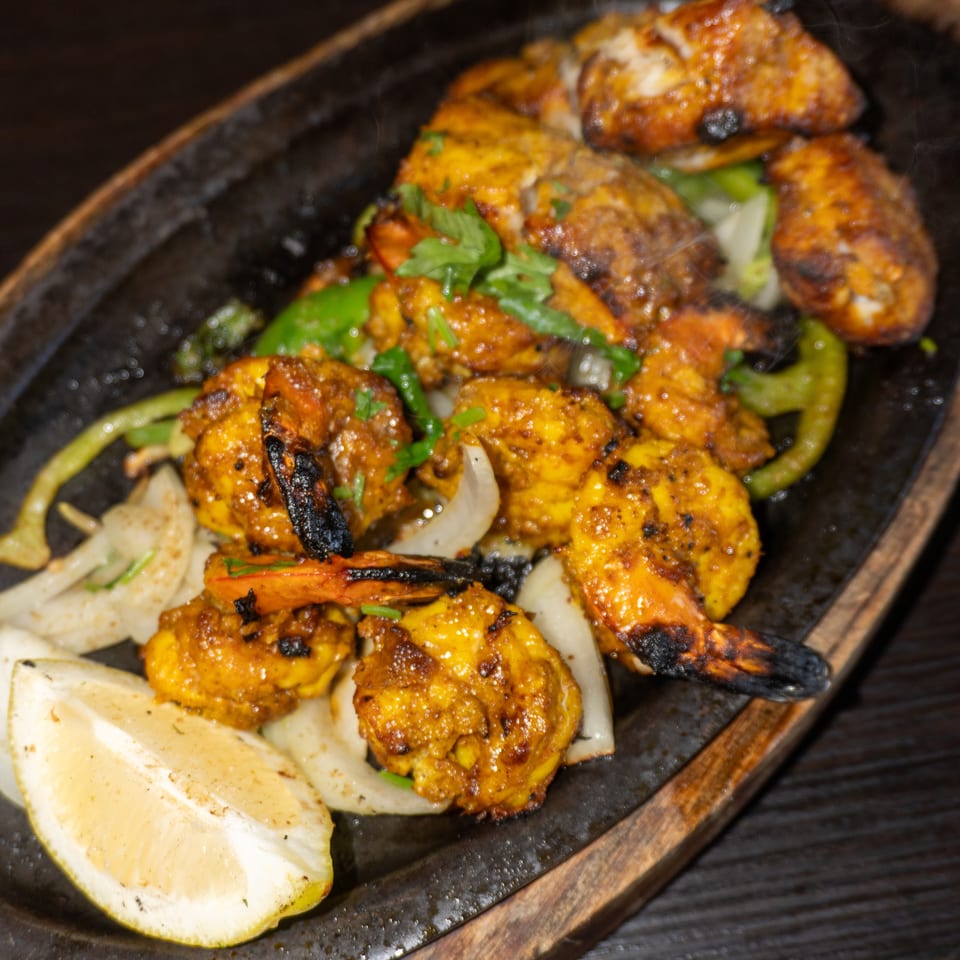 Sizzling platter of grilled shrimp and chicken with onions, peppers, and a lemon wedge.