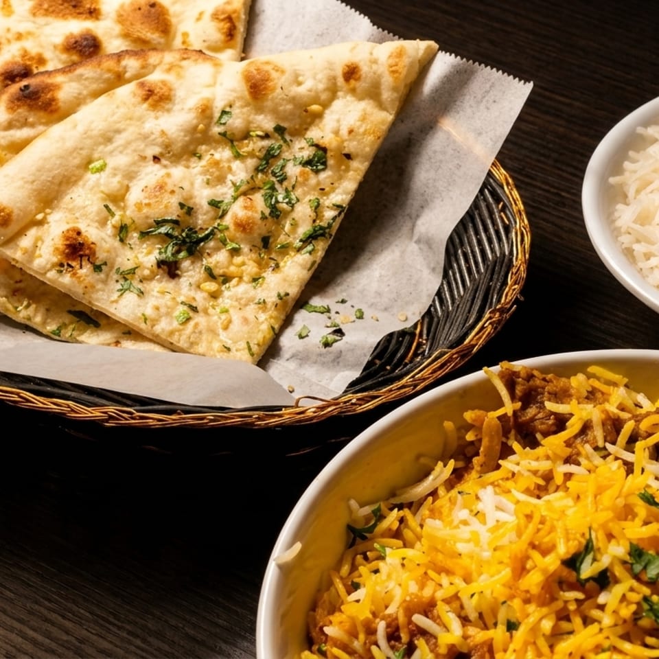 A basket of naan bread, a bowl of white rice, and a bowl of biryani with meat.