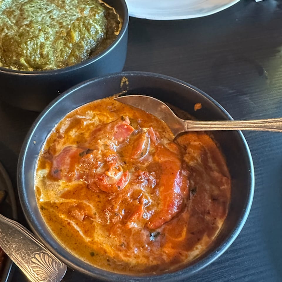 Two bowls of Indian food, one with orange curry and the other with green spinach dish.