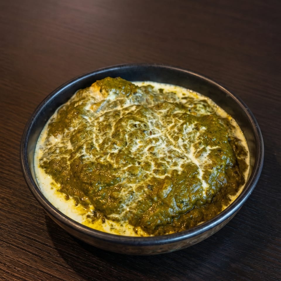A dark bowl of vibrant green palak paneer with swirls of white cream on a dark wooden table.
