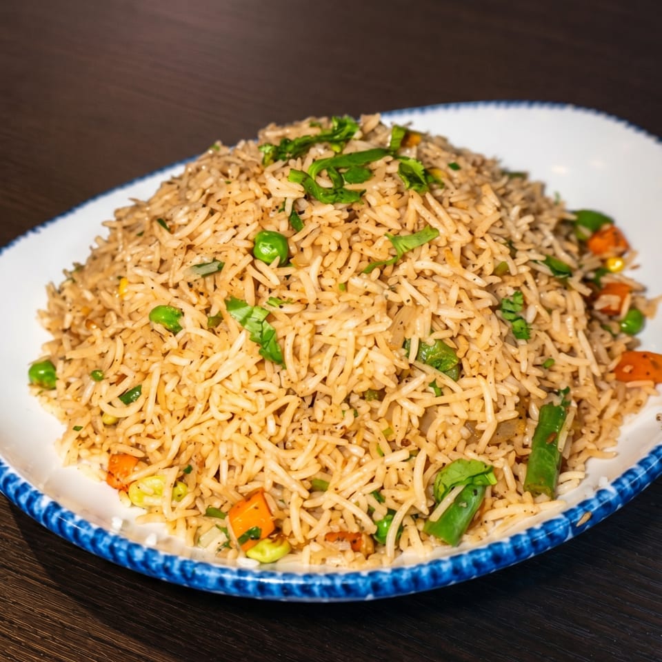 A large serving of vegetable fried rice with peas, carrots, and green onions on a white and blue plate.