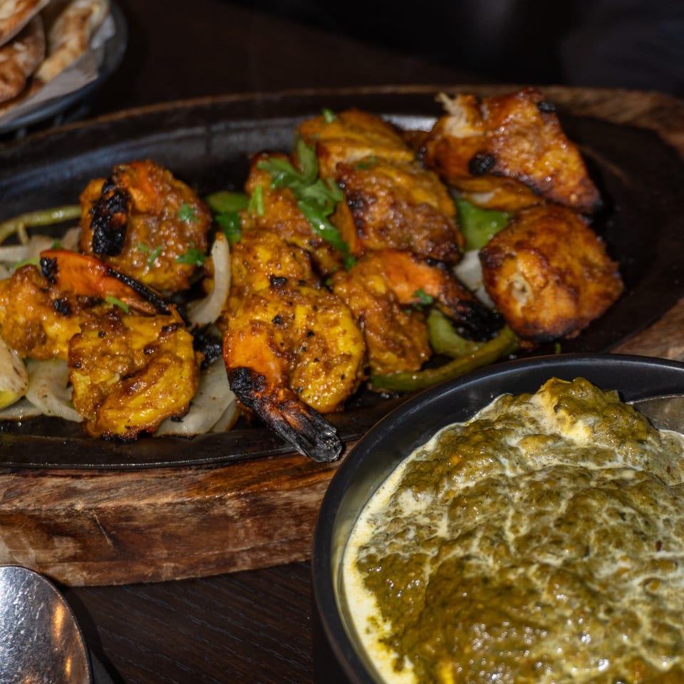 Sizzling platter of chicken and shrimp tikka with a side of creamy green saag.